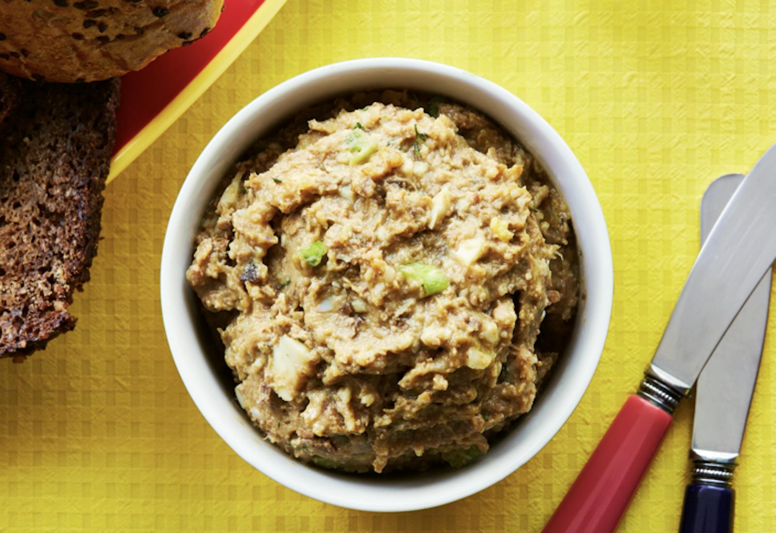 Chopped liver with slices of seeded bread atop yellow tablecloth.