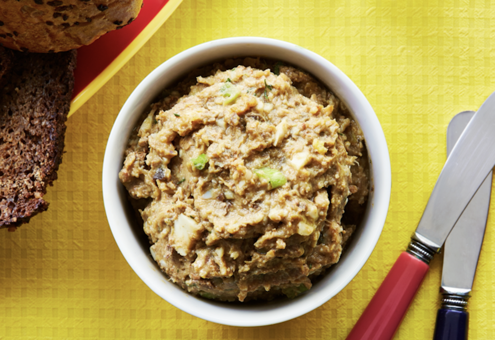 Chopped liver with slices of seeded bread atop yellow tablecloth.