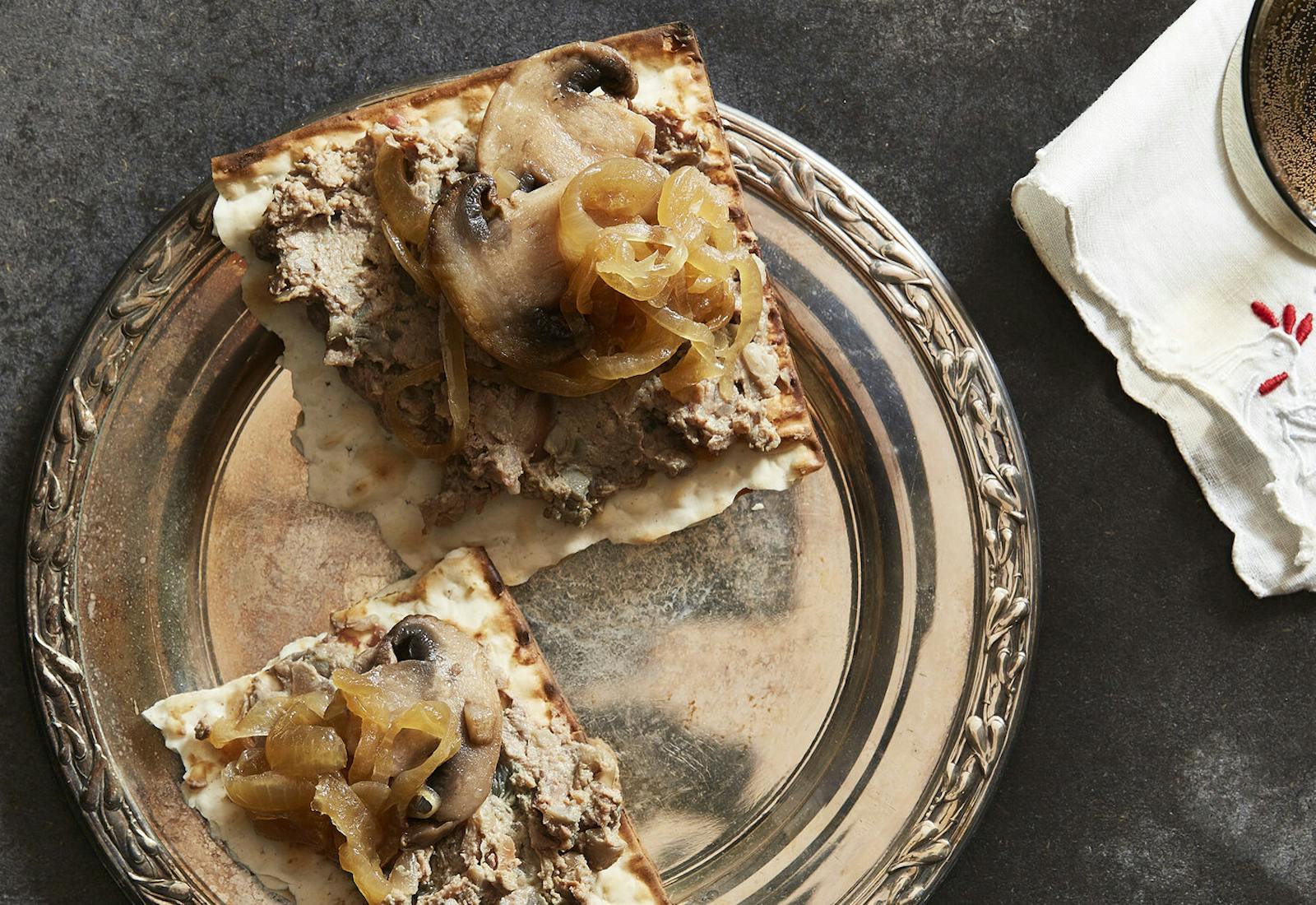 Chopped liver with mushrooms and onions on matzo bread, atop grey surface.