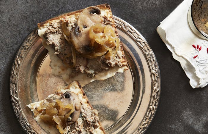 Chopped liver with mushrooms and onions on matzo bread, atop grey surface.