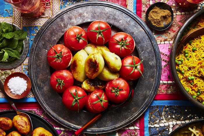 Mahasha on bronze platter alongside dishes of spice mix, coarse salt and mint atop vibrant tablecloth.