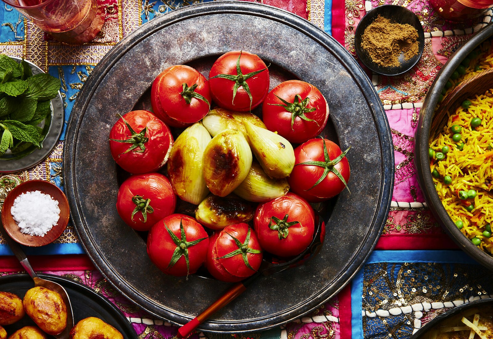Mahasha on bronze platter alongside dishes of spice mix, coarse salt and mint atop vibrant tablecloth.