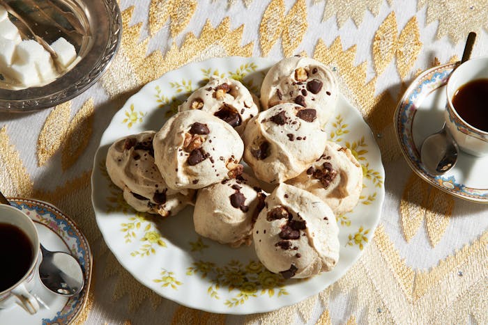 Meringues with sugar cubes and teacups atop gold tablecloth. 