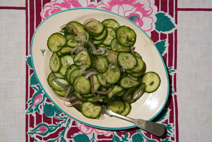 Pickled cucumber salad on green rimmed plate atop colorful tablecloth.