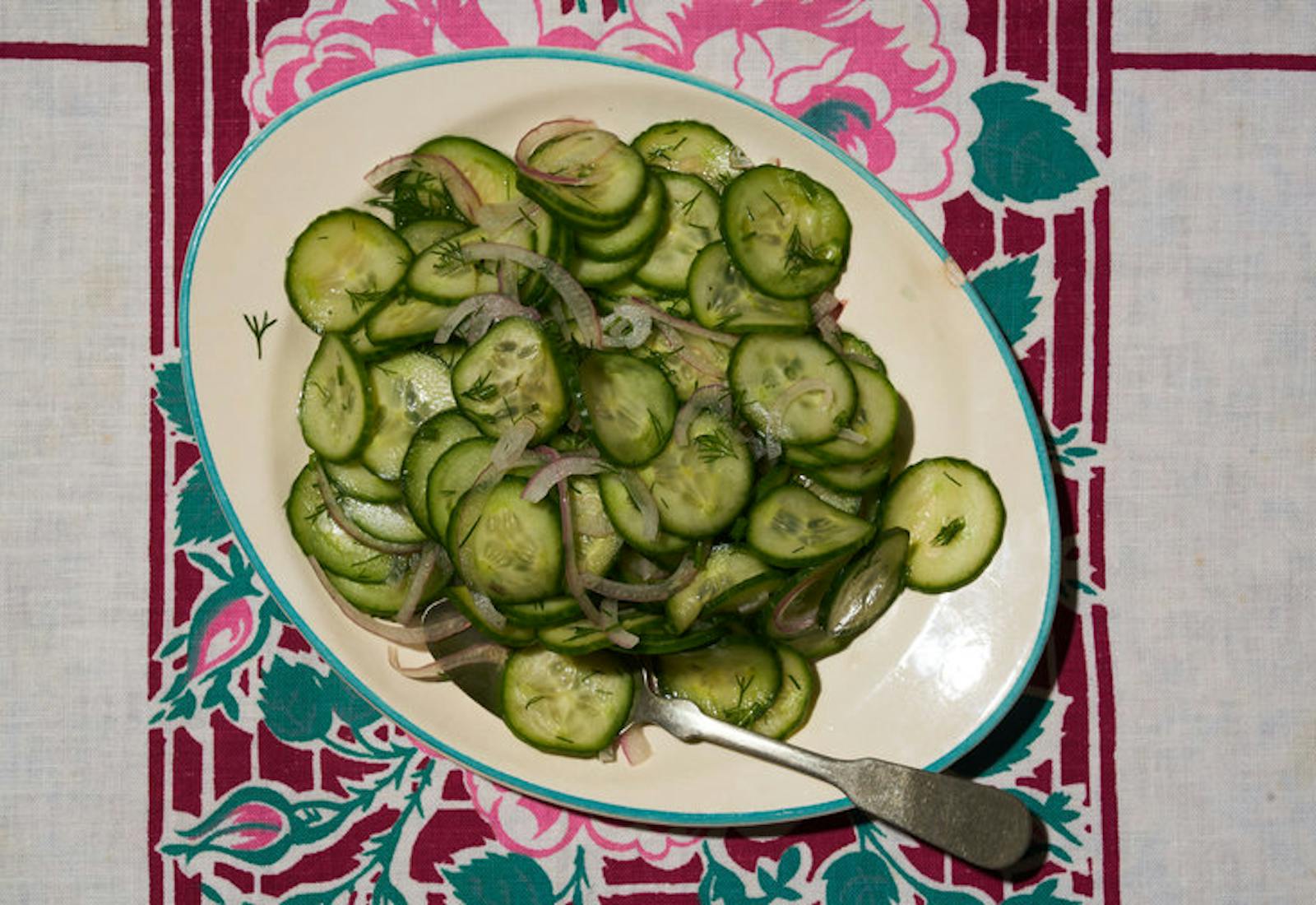 Pickled cucumber salad on green rimmed plate atop colorful tablecloth.