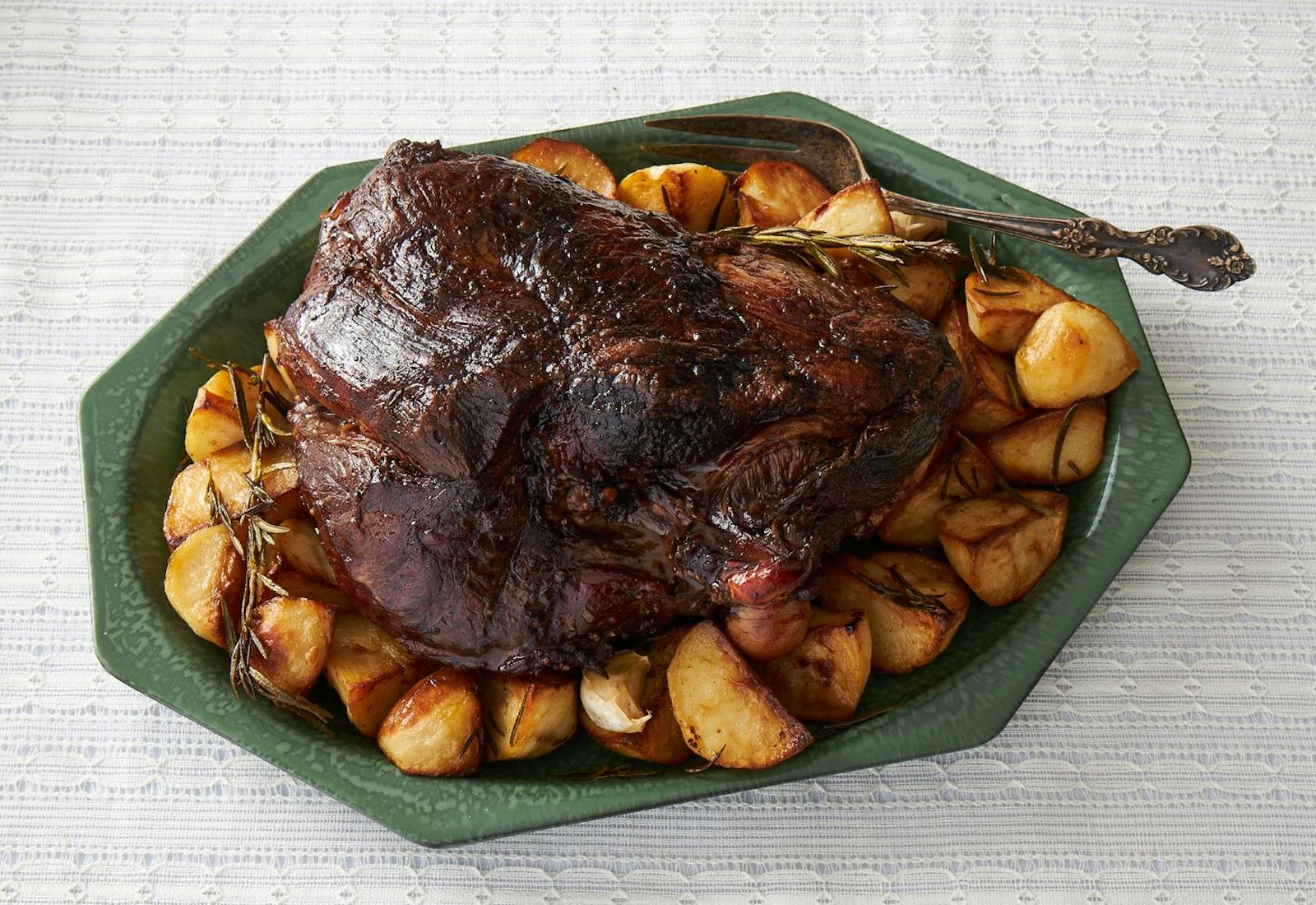 Roasted lamb shoulder with herbs and potatoes, green serving dish.