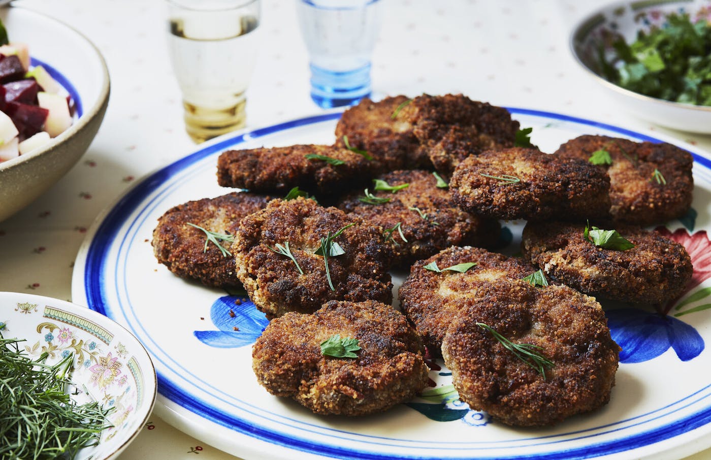 Kotlety with parsley and dill, glasses of vodka and bowls of herbs.