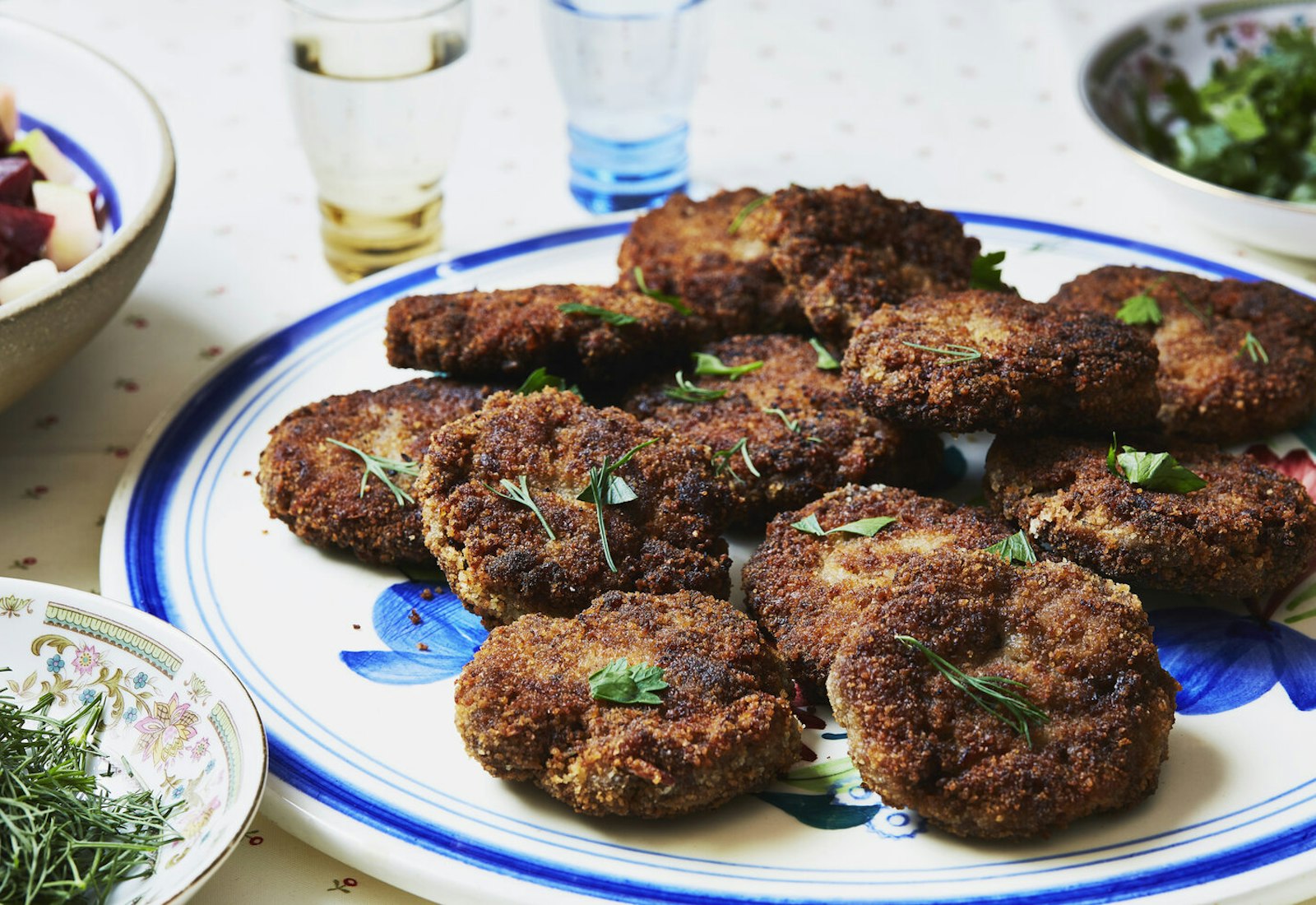 Kotlety with parsley and dill, glasses of vodka and bowls of herbs.