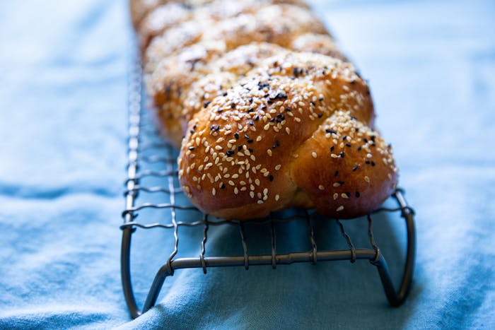 Loaf of challah on wire rack atop blue tablecloth. 