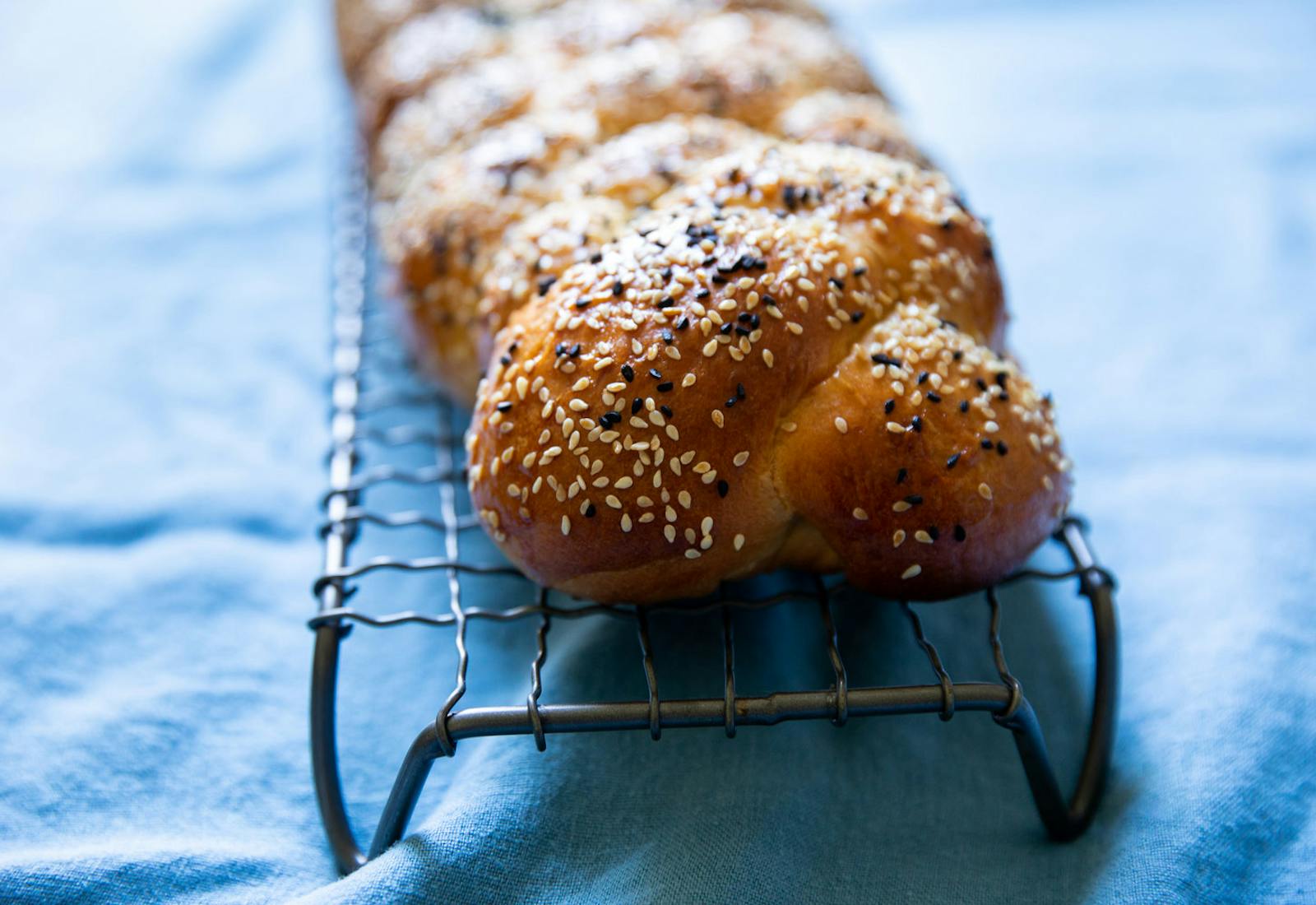 Loaf of challah on wire rack atop blue tablecloth. 