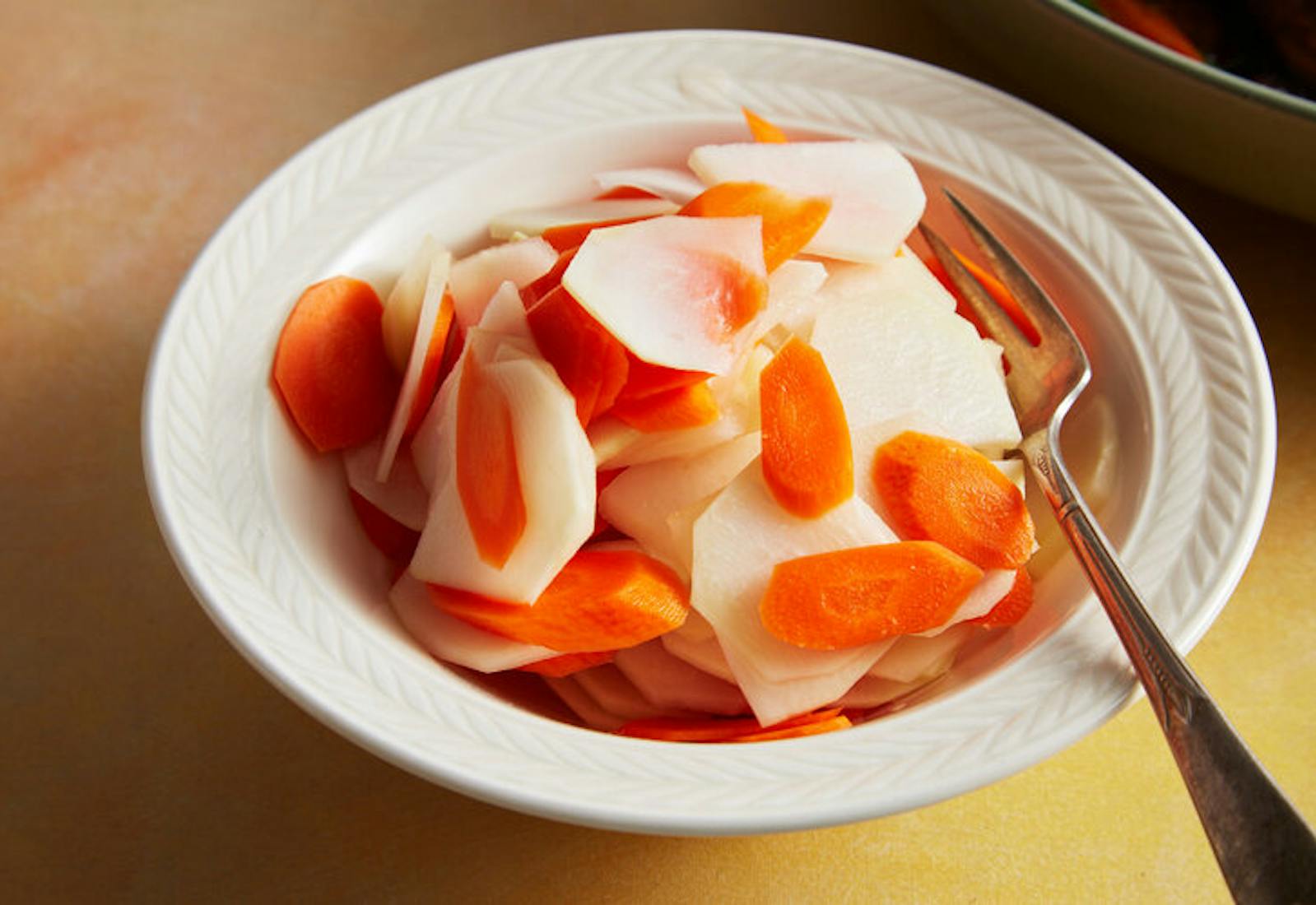 Kohlrabi and carrot salad in white bowl atop yellow surface.