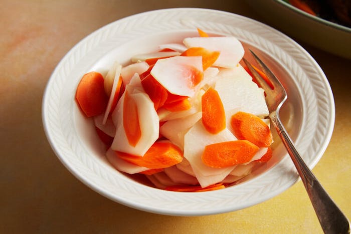 Kohlrabi and carrot salad in white bowl atop yellow surface.