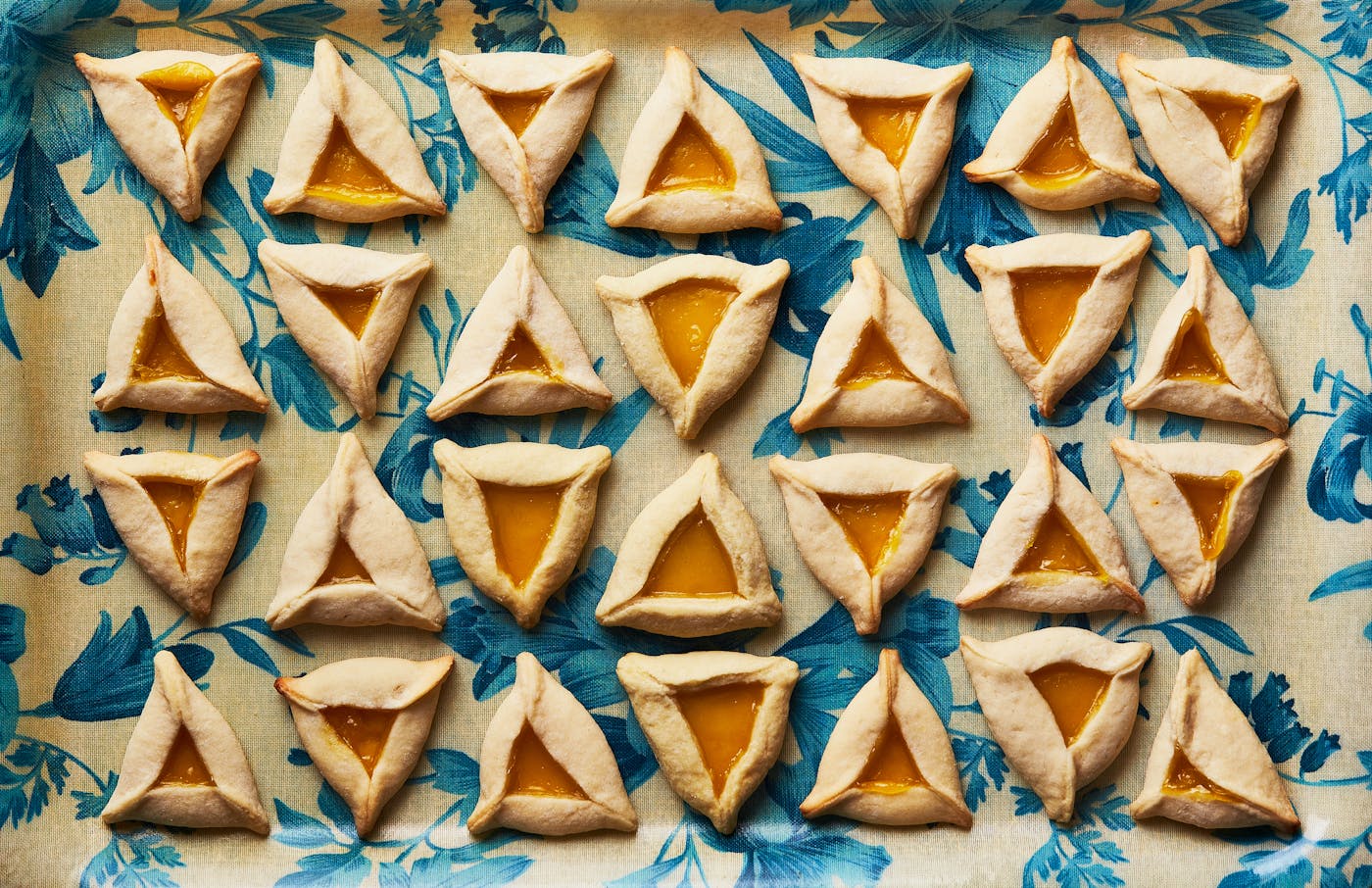 Lemon curd-filled hamantaschens on blue floral dish.