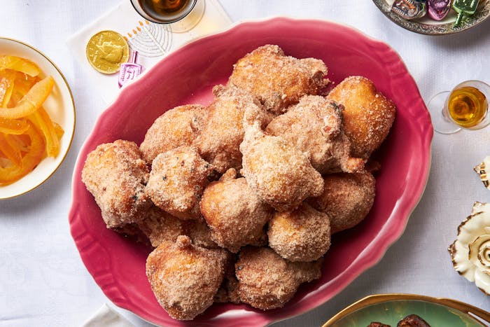 Frittole dolci with gelt, dreidels, wine and flowers atop white tablecloth.