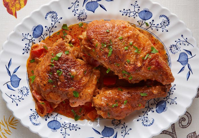Chicken paprikas sprinkled with chopped parsley on blue-patterned plate, atop white tablecloth.