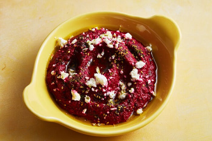 Spiced beet dip with crumbled feta in yellow dish atop yellow surface.