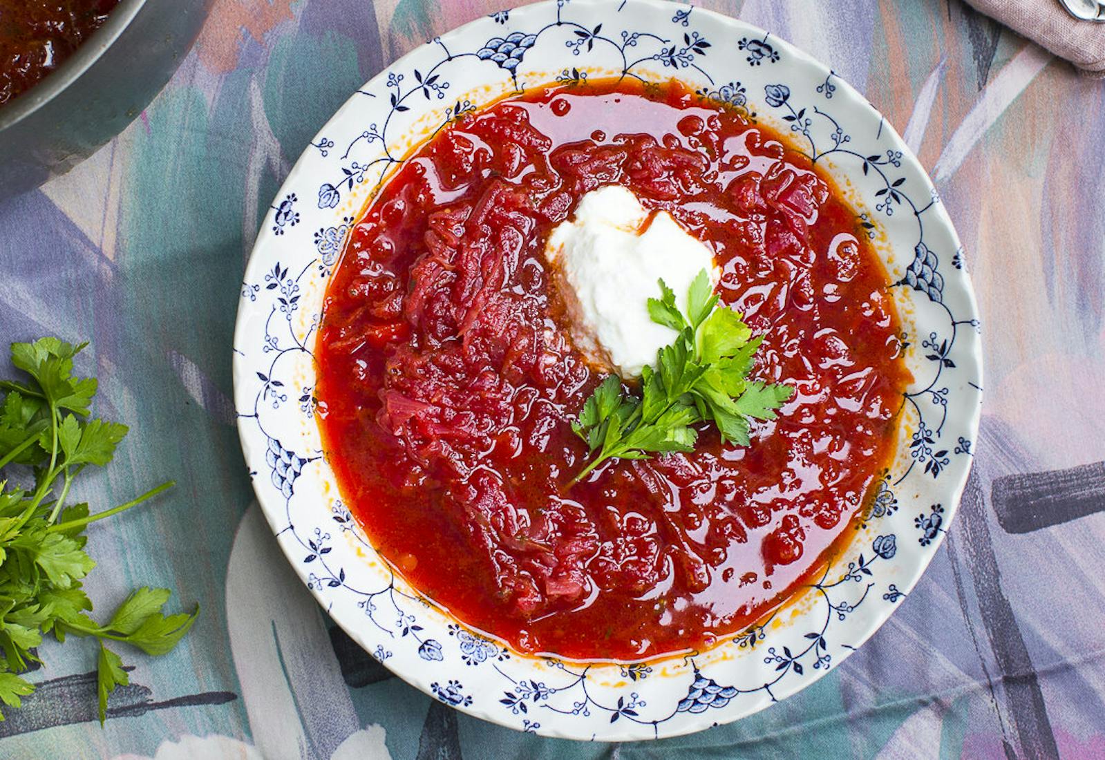 Borscht with dollop of sour cream and parsley alongside vegetarian borscht atop colorful tablecloth.