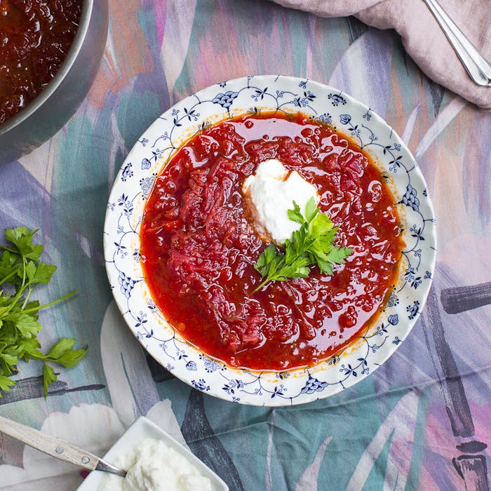 Borscht with dollop of sour cream and parsley alongside vegetarian borscht atop colorful tablecloth.