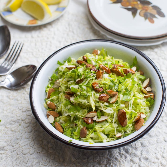 Cabbage salad with chopped almonds alongside dish with lemon wedges atop white tablecloth.