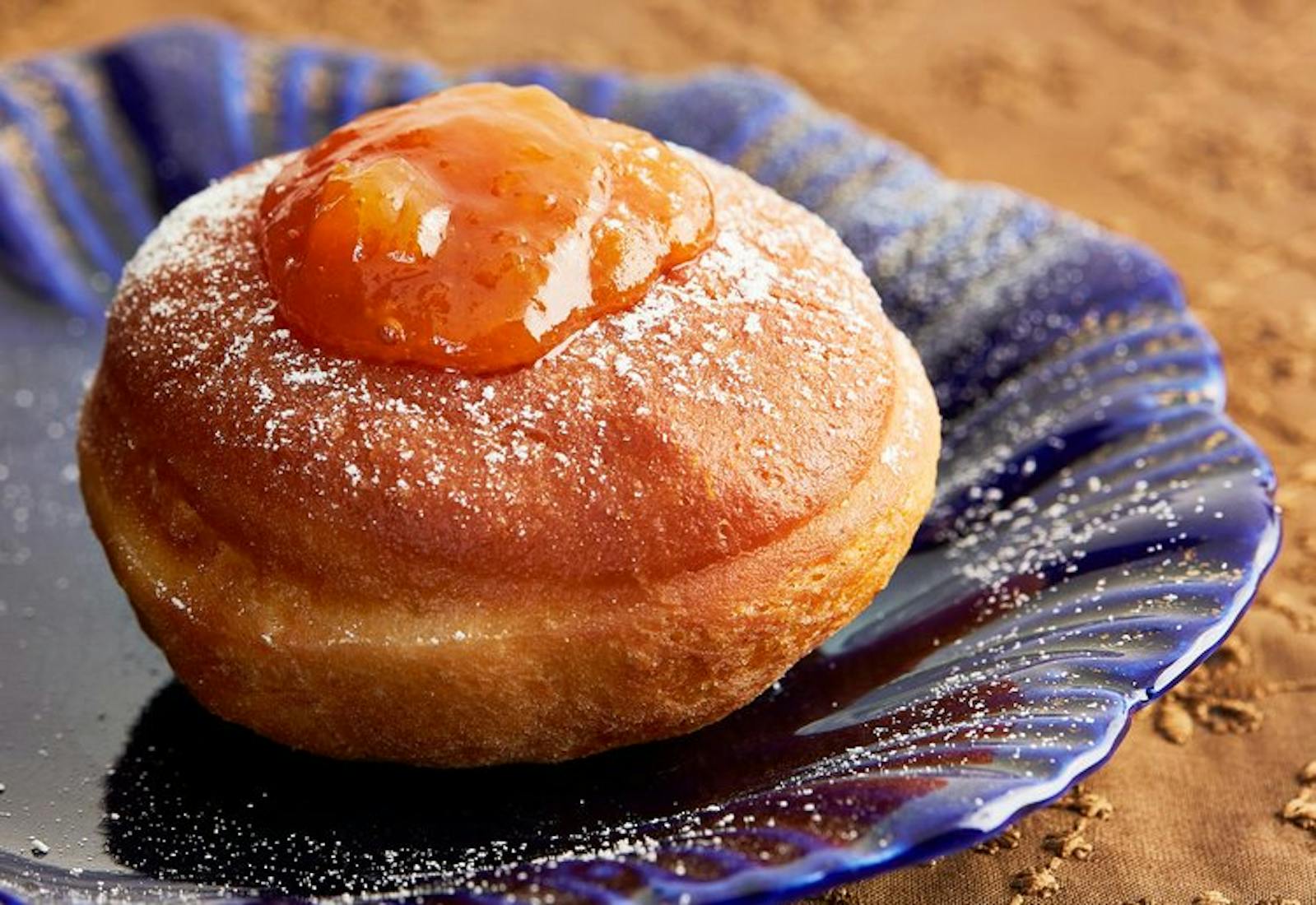 Doughnut with dollop of apricot jam and powdered sugar on blue plate.