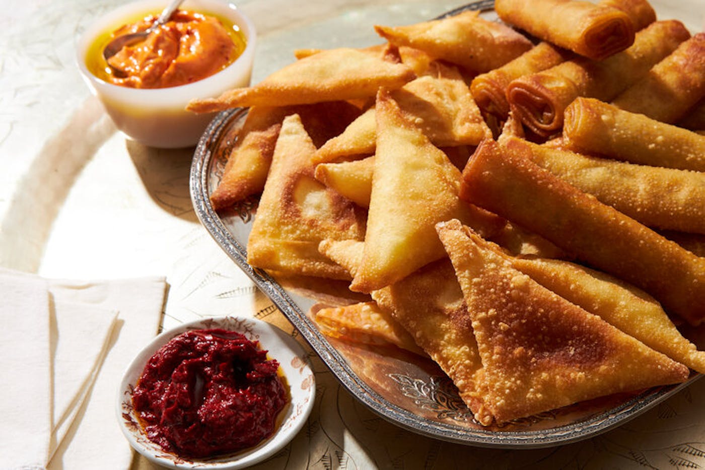 Beef cigars on serving tray, small bowls with harissa aioli and harissa paste.