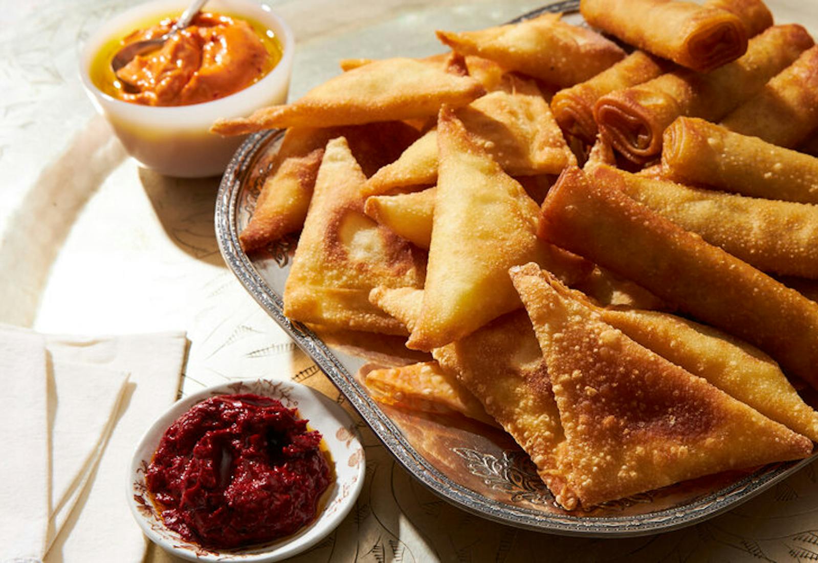 Beef cigars on serving tray, small bowls with harissa aioli and harissa paste.