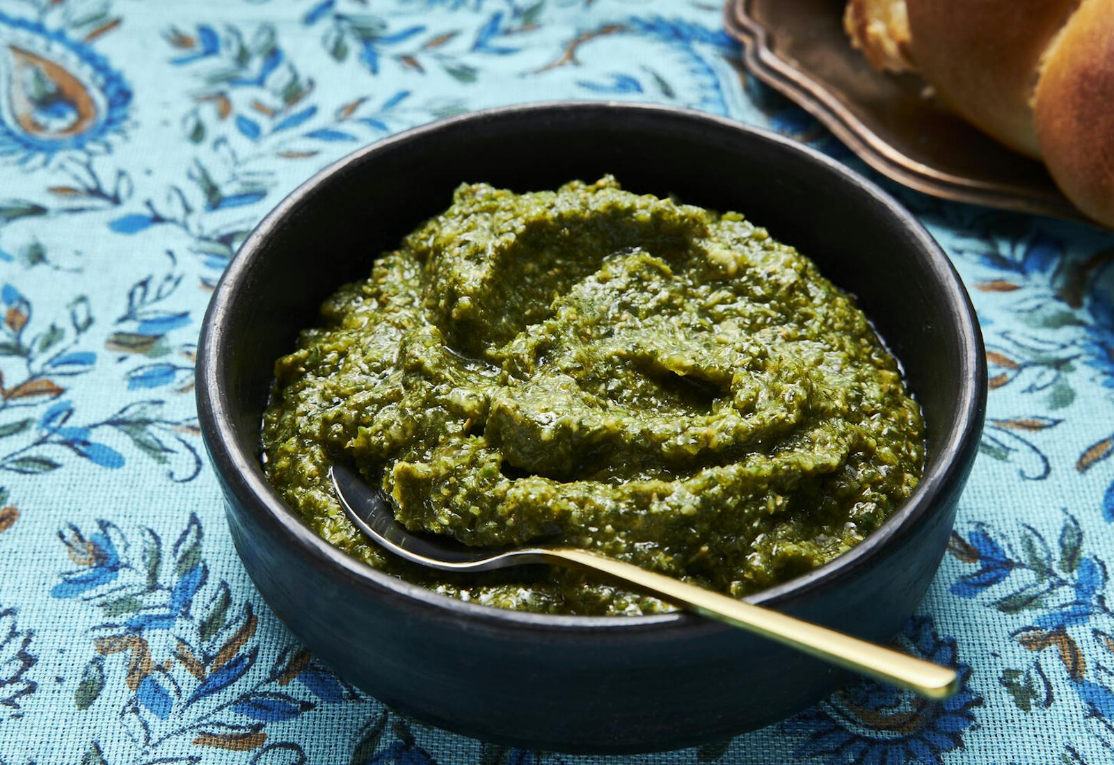 Halba in black dish alongside loaf of challah atop blue feather-printed tablecloth.
