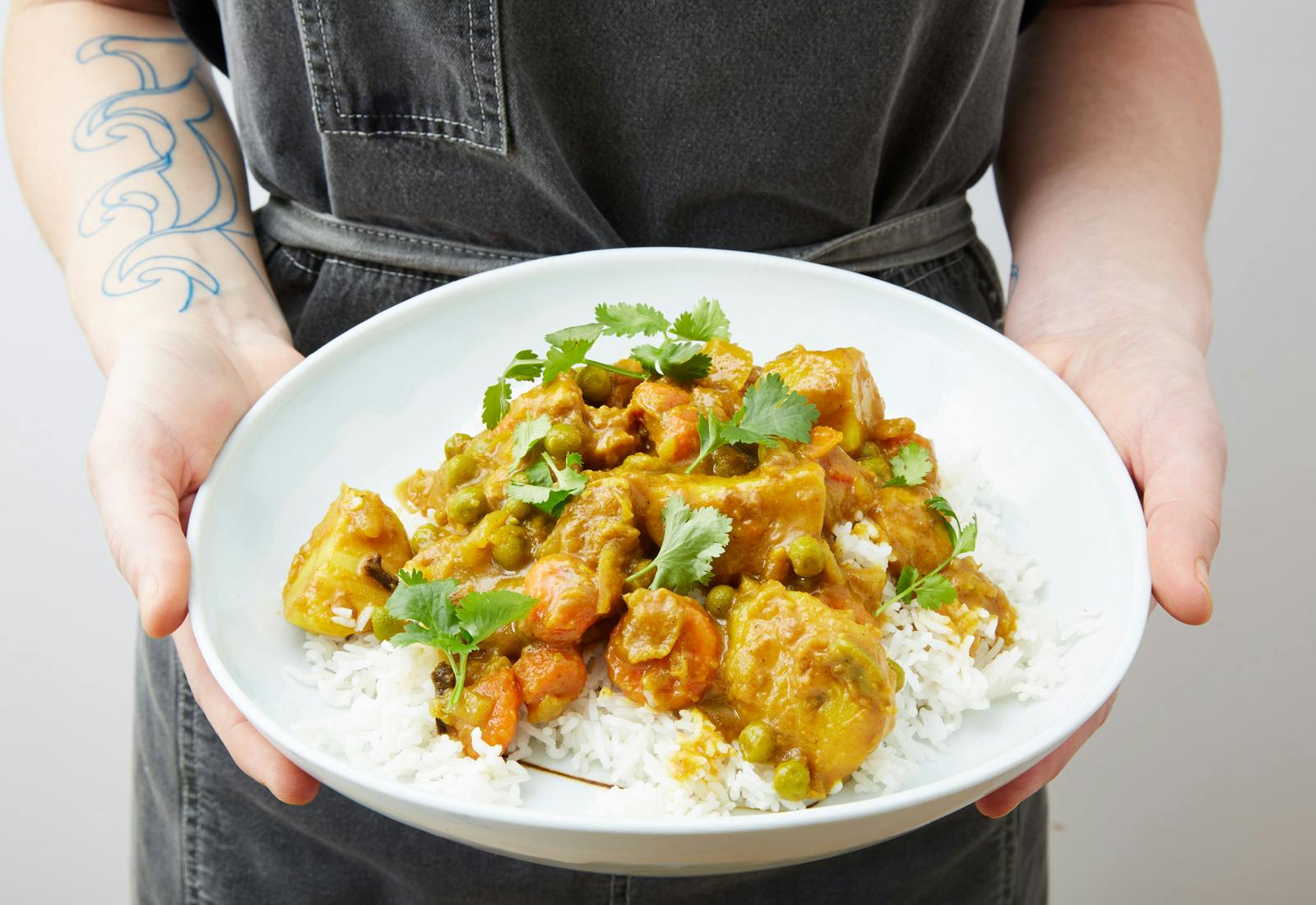 Chef holding chicken curry over white rice garnished with cilantro in white bowl.