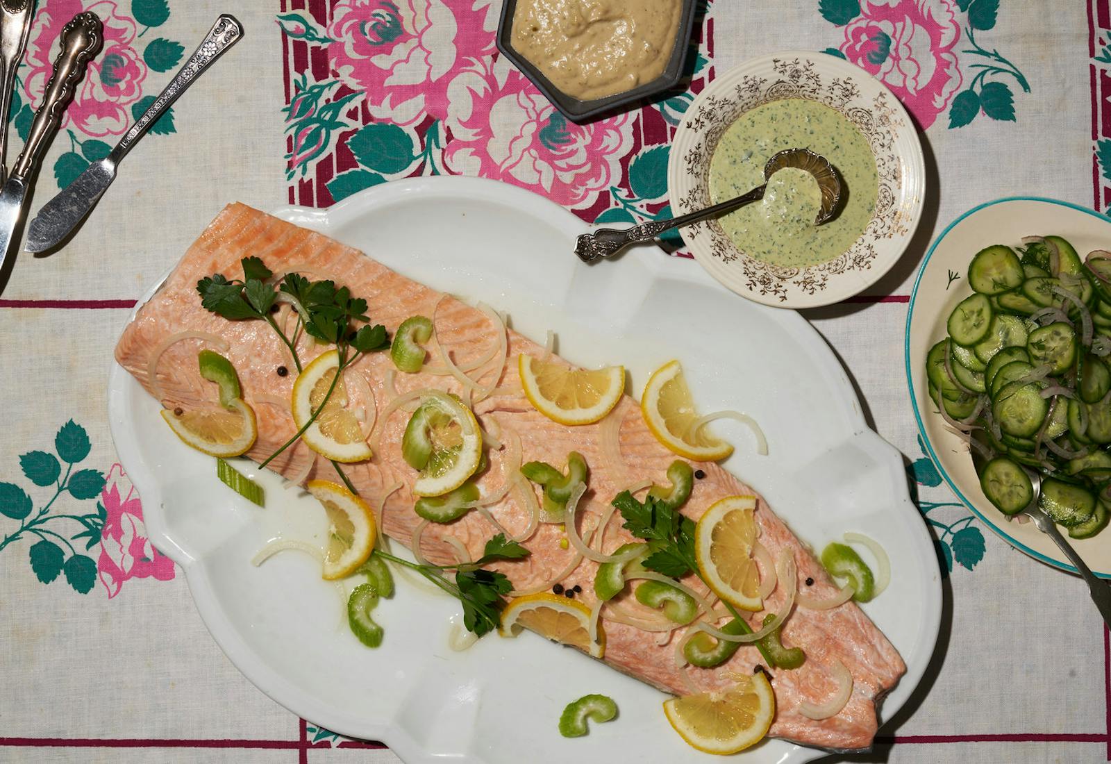 Poached salmon garnished with lemon wedges, celery and parsley alongside tonnato sauce, sauce vert and cucumber salad. 