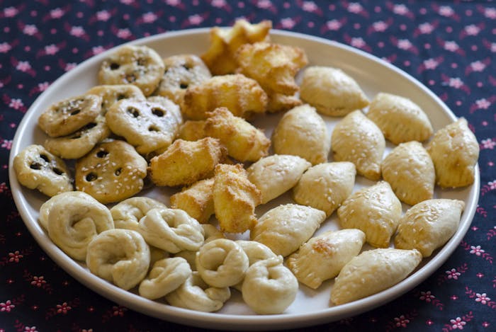 Spread of Iraqi Purim treats: hadgi coconut, cheese sambusak, k'aakat, be'be tamer (clockwise from top center of bowl).