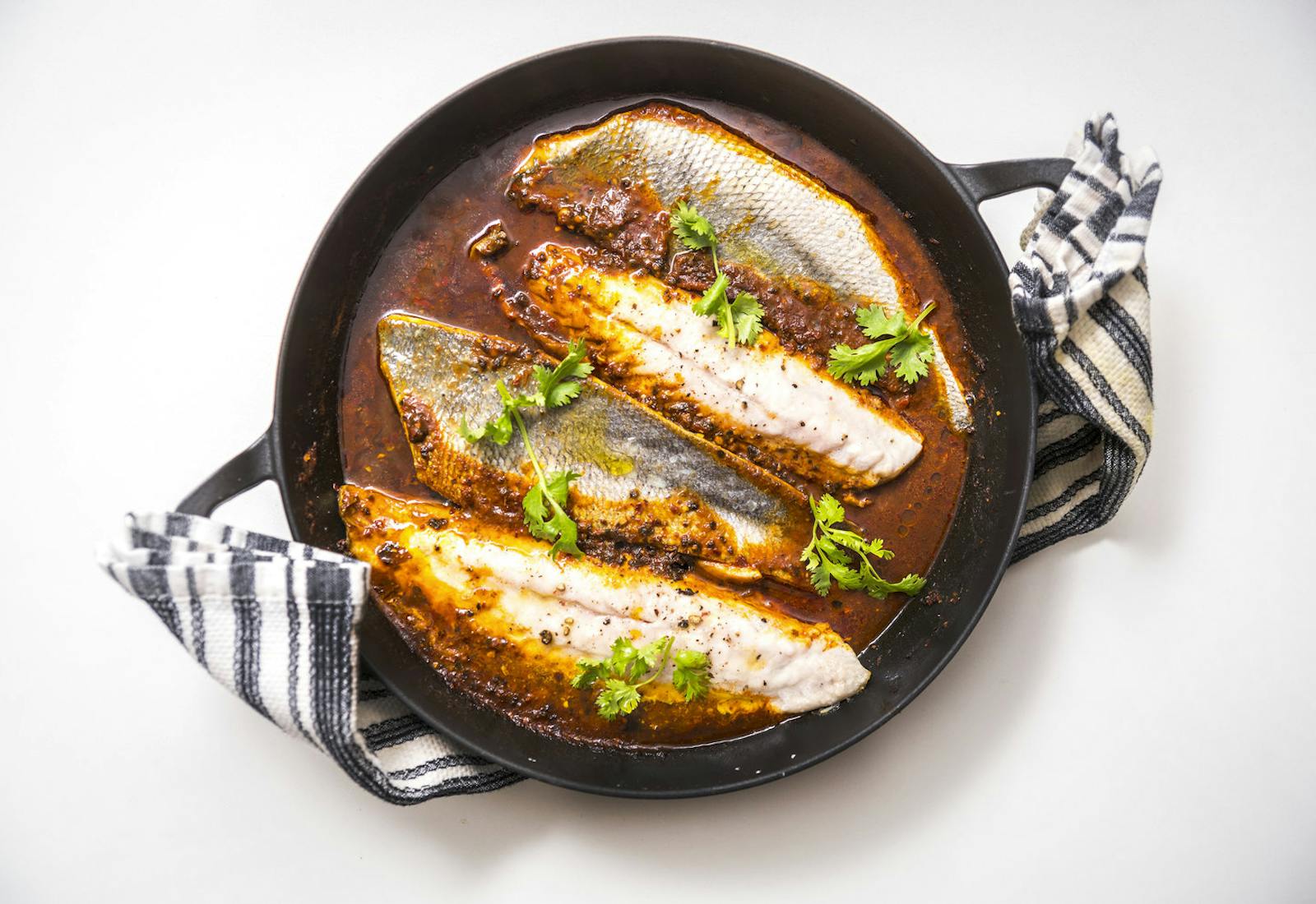 Chraime in cast iron skilled garnished with cilantro atop striped napkin.