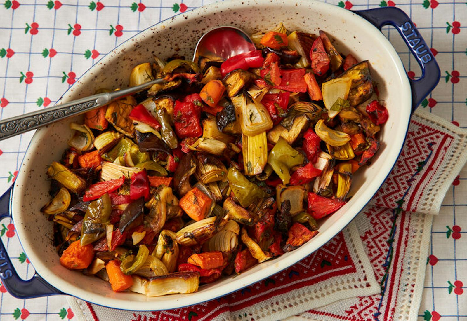 Guvetch in large dutch oven atop festive napkin and fruit-patterned tablecloth.