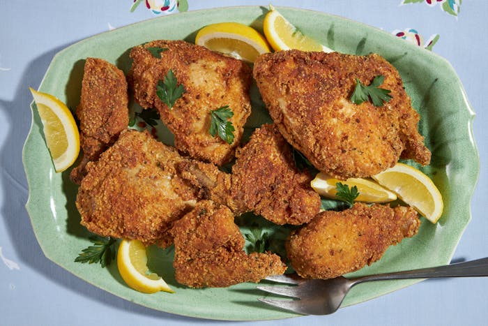 Fried chicken with parsley and lemon wedges on green platter, atop blue tablecloth.