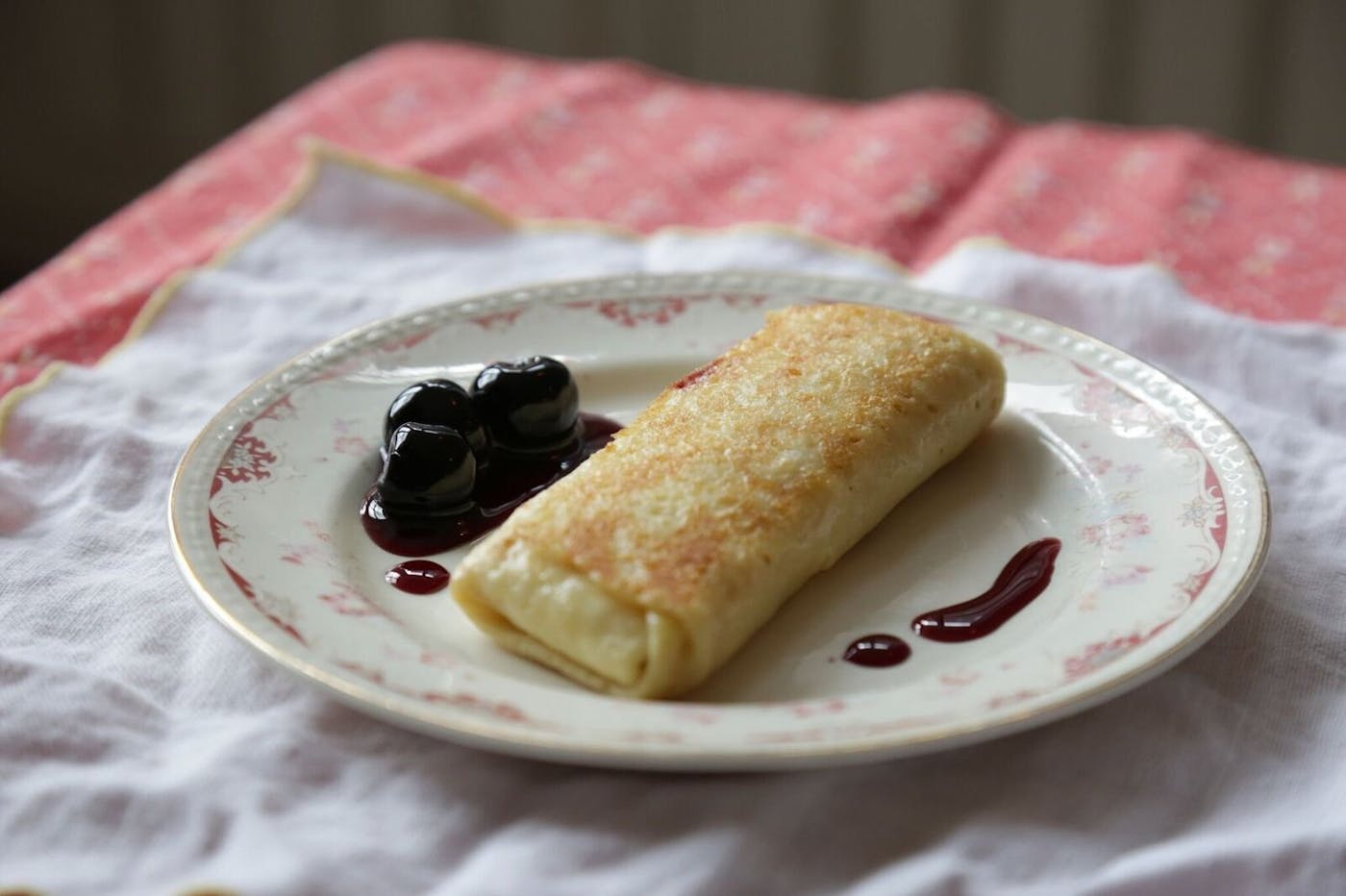 Cheese blintzes with dollop of cherry compote on small dish atop white and pink cloths.