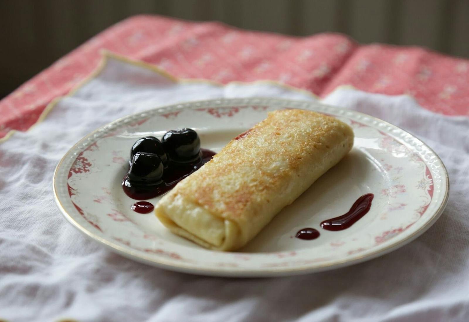 Cheese blintzes with dollop of cherry compote on small dish atop white and pink cloths.