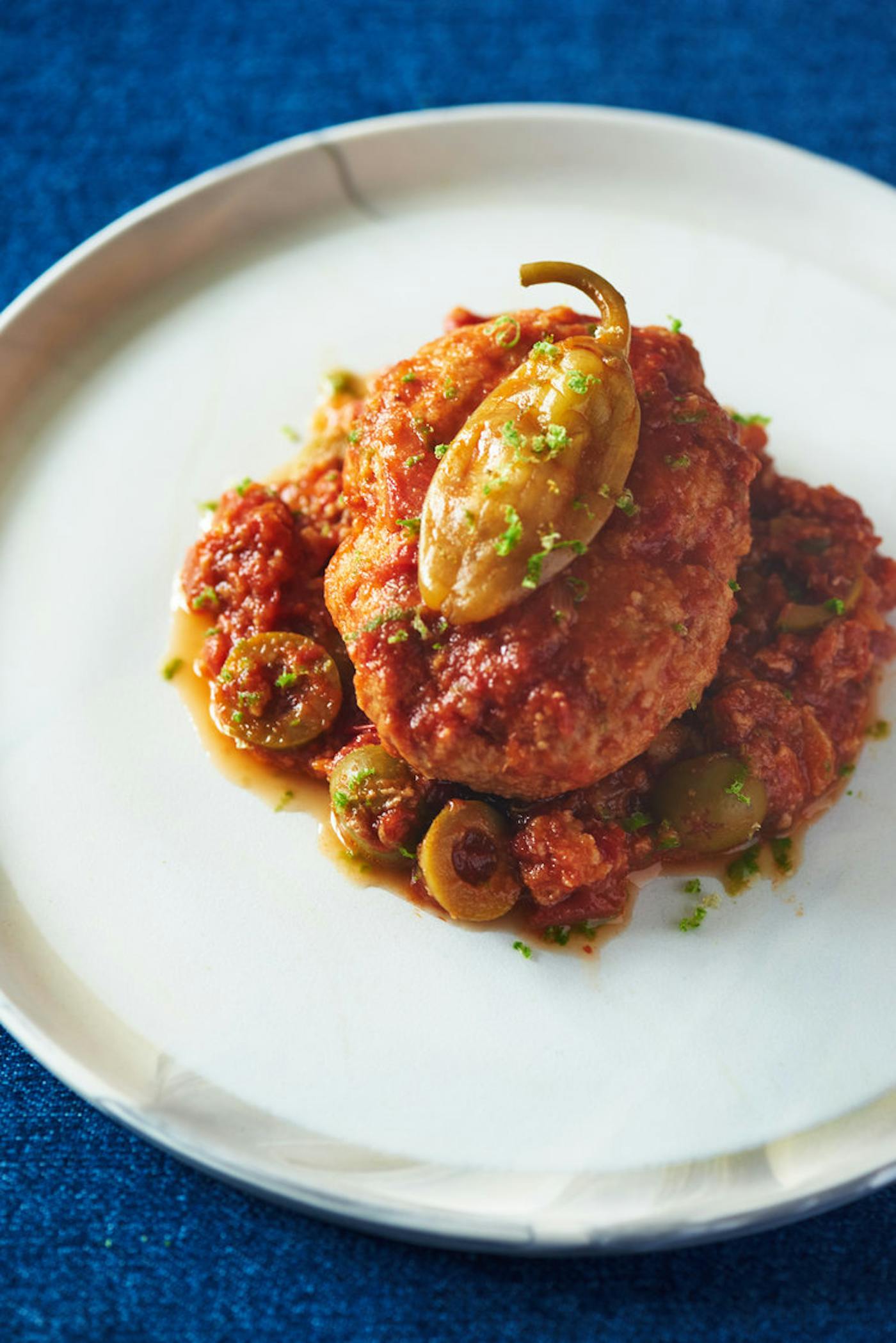Gefilte fish a la Veracruzana on white plate atop blue tablecloth.