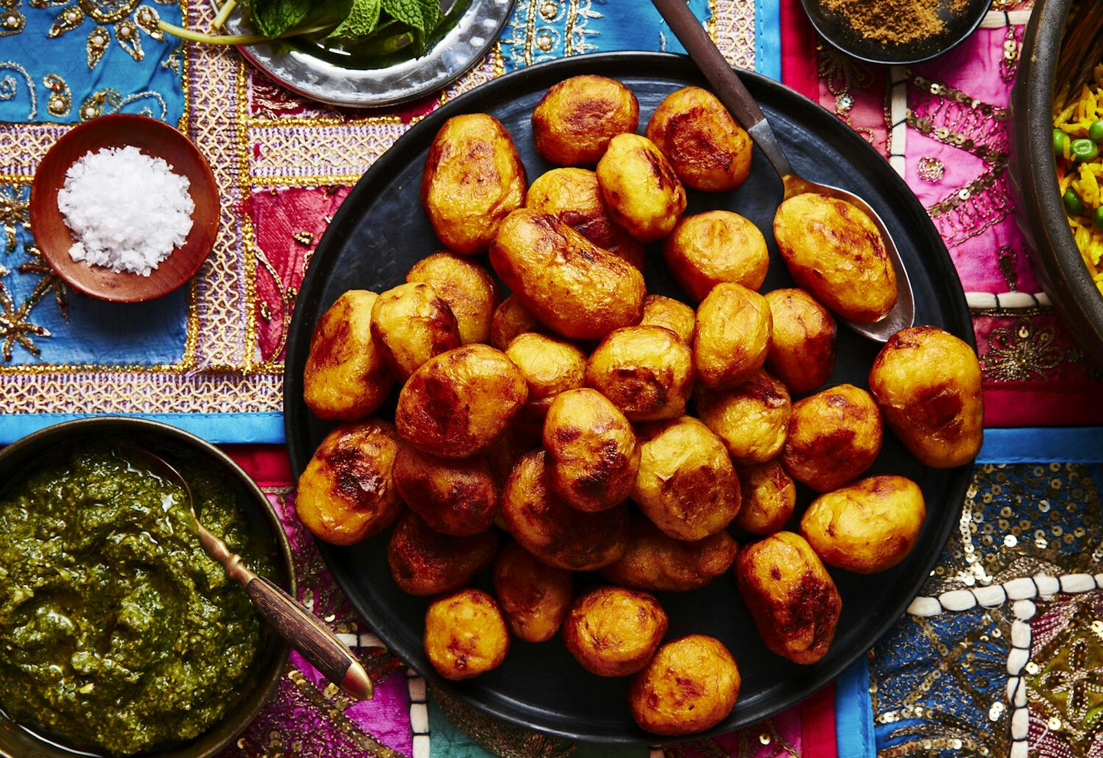 Aloo makala on black plate alongside dishes of mint, course salt, spice mix and halba.