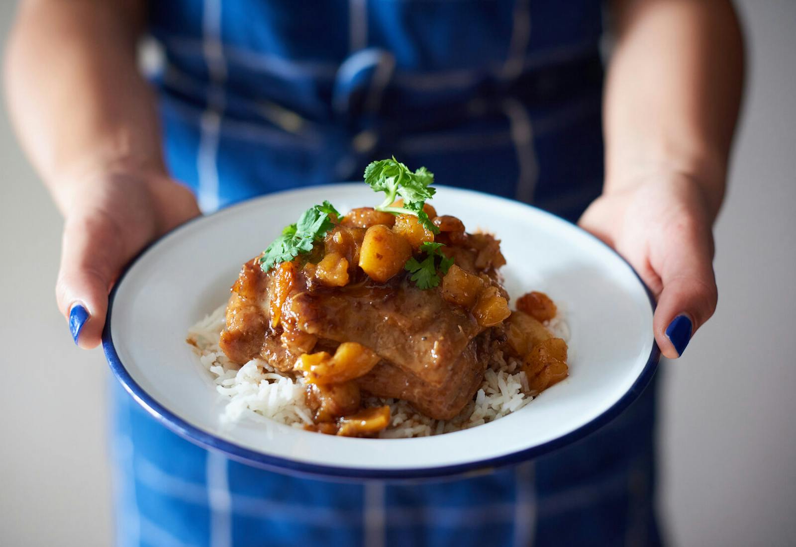 Chef holding pollo con salsa garnished with cilantro on bed of white rice.
