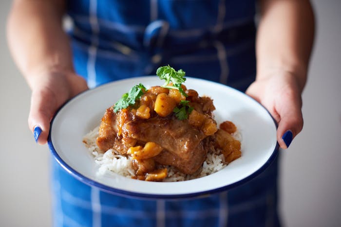 Chef holding pollo con salsa garnished with cilantro on bed of white rice.