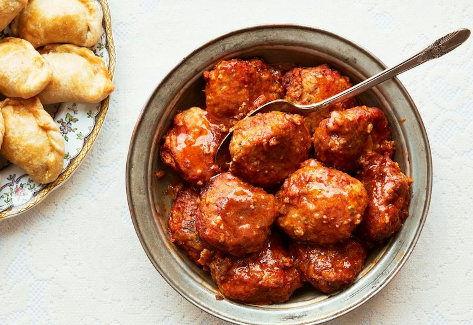 Keftes in metal bowl with serving spoon, bourekas on side.