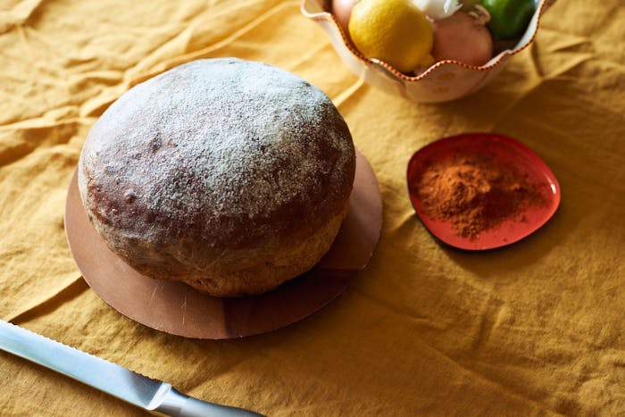 Dabo on wooden plate, dish of berbere spice mix, bowl with lemons and onions atop yellow tablecloth.