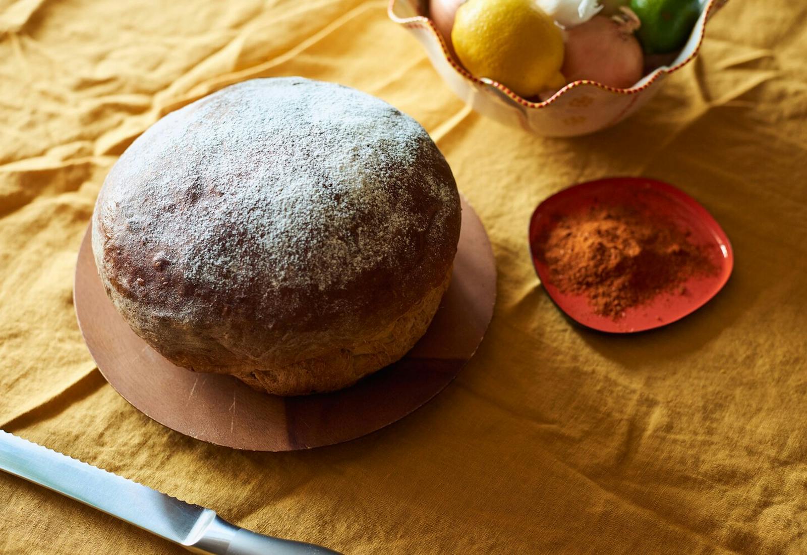 Dabo on wooden plate, dish of berbere spice mix, bowl with lemons and onions atop yellow tablecloth.