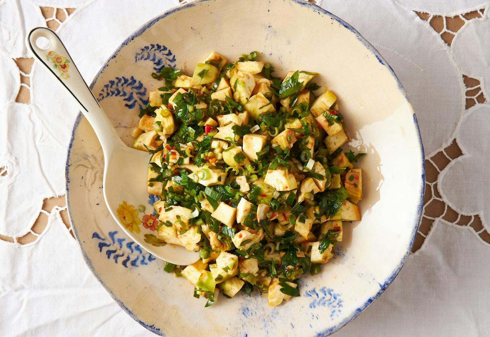 Artichoke salad in serving bowl atop white tablecloth. 