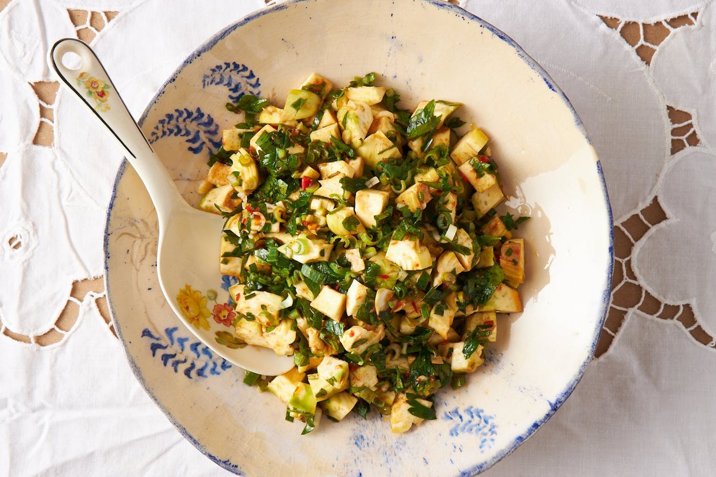 Artichoke salad in serving bowl atop white tablecloth. 