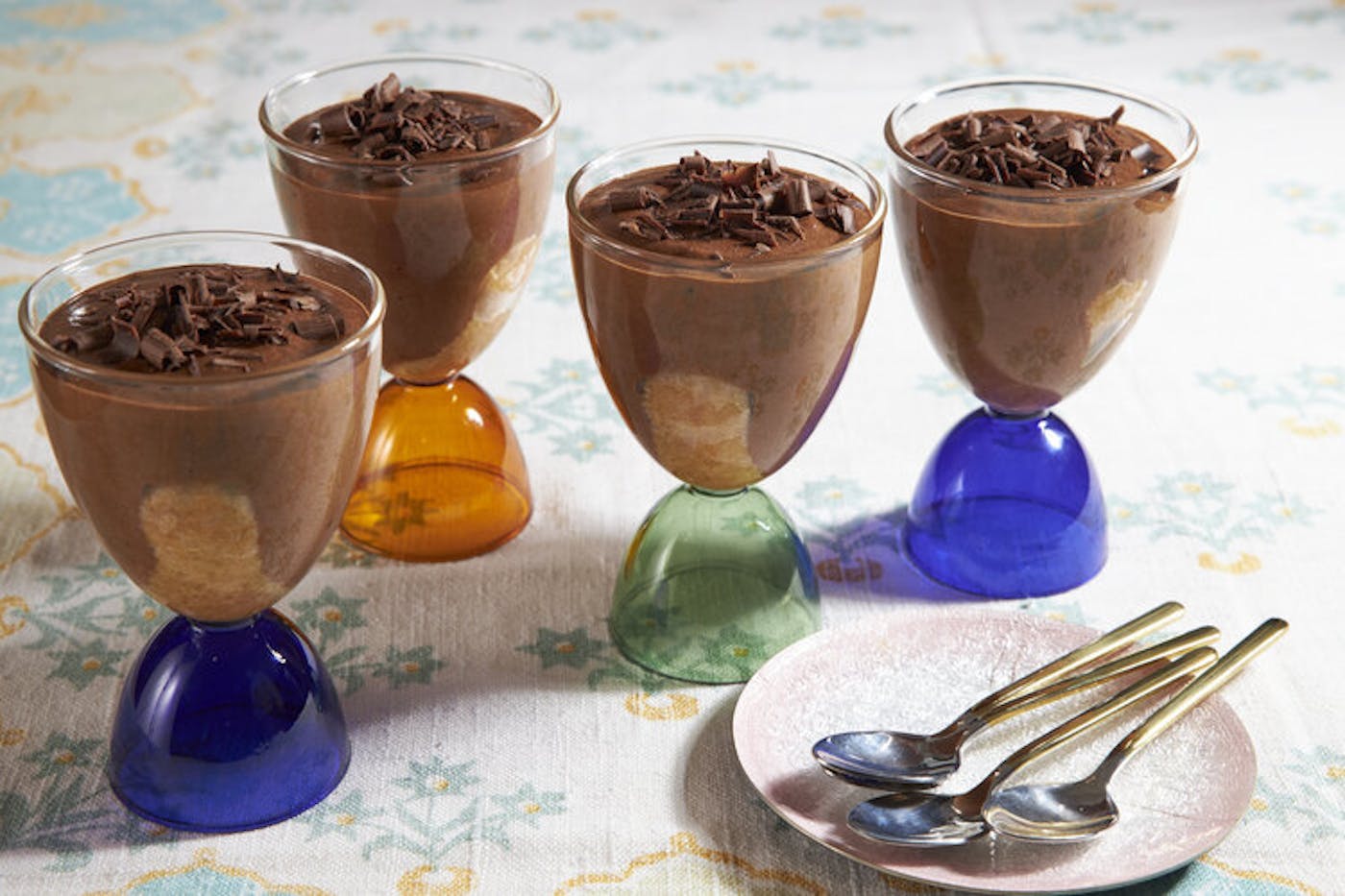 Chocolate mousse in ice cream glasses with spoons, atop pale patterned tablecloth.