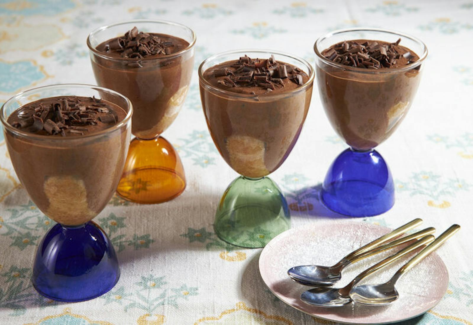 Chocolate mousse in ice cream glasses with spoons, atop pale patterned tablecloth.