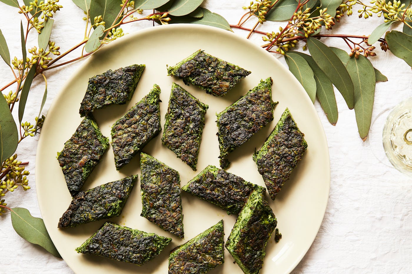 Diamonds of kuku sabzi alongside glass of white wine.