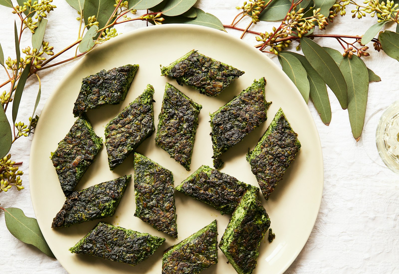 Diamonds of kuku sabzi alongside glass of white wine.