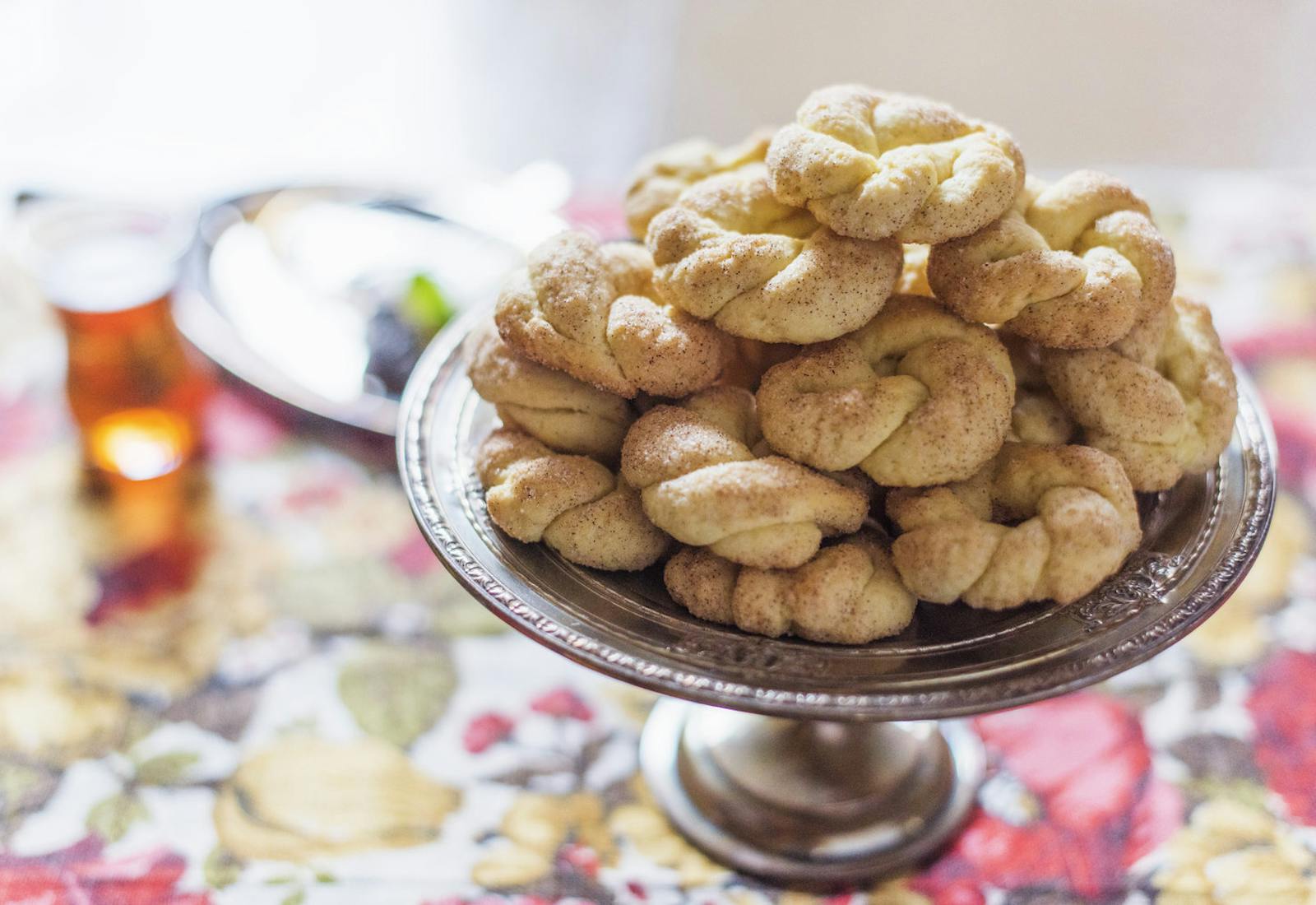 Biscochos dipped in cinnamon sugar on metal platter atop floral tablecloth.