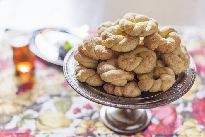 Biscochos dipped in cinnamon sugar on metal platter atop floral tablecloth.